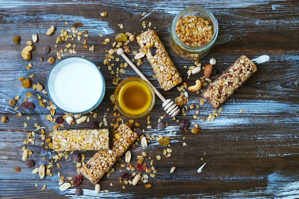 Cereal bars with dry fruits, nuts, granola and glass of milk on wooden background.Top view.