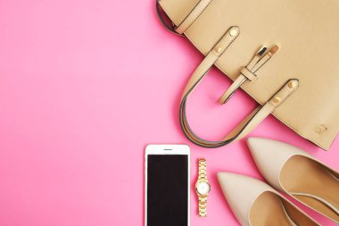 Kadınsı aksesuarları düz yatıyordu. Kadın Ayakkabı, çanta, smartphone ve pembe bir arka plan nöbette. Bej renk kadın aksesuarları. Metin alanı. Üstten Görünüm.  
