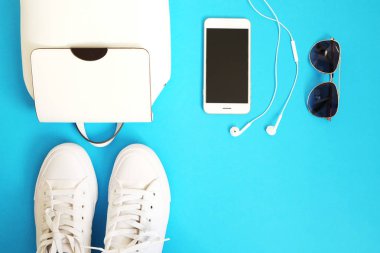 Kadınsı aksesuarları düz yatıyordu. Kadın Ayakkabı, çanta, smartphone ve pembe bir arka plan nöbette. Bej renk kadın aksesuarları. Metin alanı. Üstten Görünüm. Mavi zemin üzerine beyaz snickers.