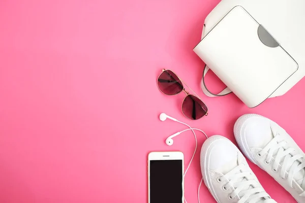 Feminine accessories flat lay. Woman shoes, bag, smartphone and watch on pink background. Beige color woman accessories. Text space. Top view.  White snickers on pink background.