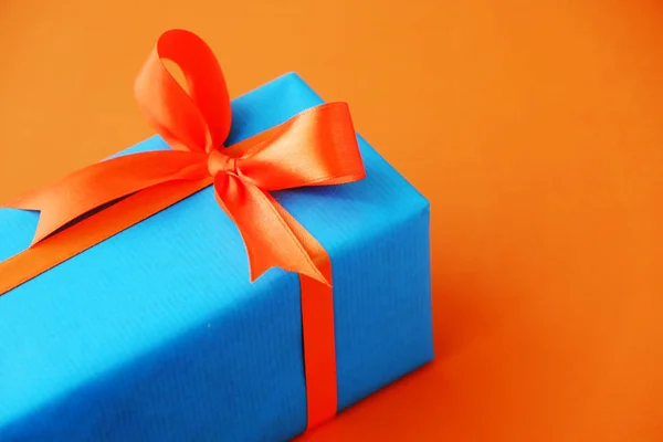 Gift or present box wrapped in blue paper and orange ribbon on color table top view. Flat lay. Copy space for text.