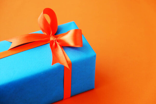 Gift or present box wrapped in blue paper and orange ribbon on color table top view. Flat lay. Copy space for text.