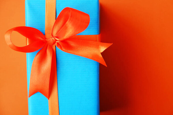 Gift or present box wrapped in blue paper and orange ribbon on color table top view. Flat lay. Copy space for text.