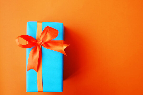 Gift or present box wrapped in blue paper and orange ribbon on color table top view. Flat lay. Copy space for text.