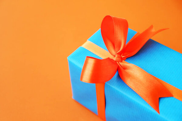 Gift or present box wrapped in blue paper and orange ribbon on color table top view. Flat lay. Copy space for text.