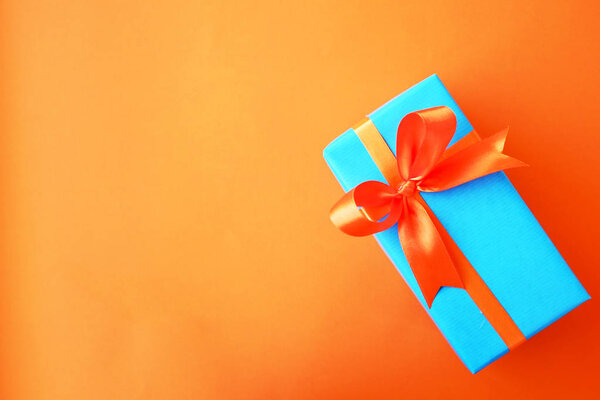 Gift or present box wrapped in blue paper and orange ribbon on color table top view. Flat lay. Copy space for text.