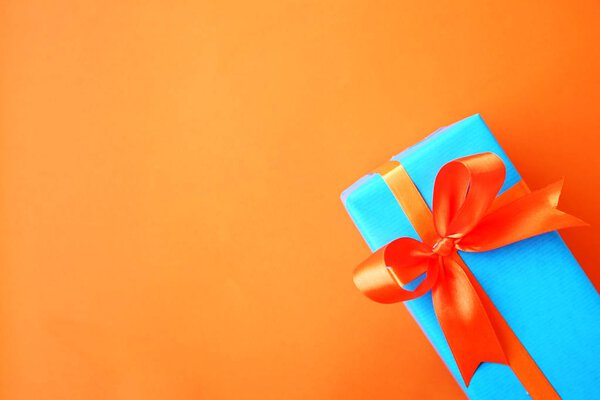 Gift or present box wrapped in blue paper and orange ribbon on color table top view. Flat lay. Copy space for text.