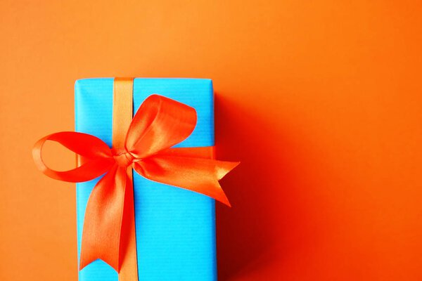 Gift or present box wrapped in blue paper and orange ribbon on color table top view. Flat lay. Copy space for text.