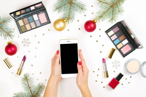 Maquillage ensemble cosmétique avec décoration de Noël et téléphone intelligent dans les mains de la femme sur fond blanc plat laïc — Photo