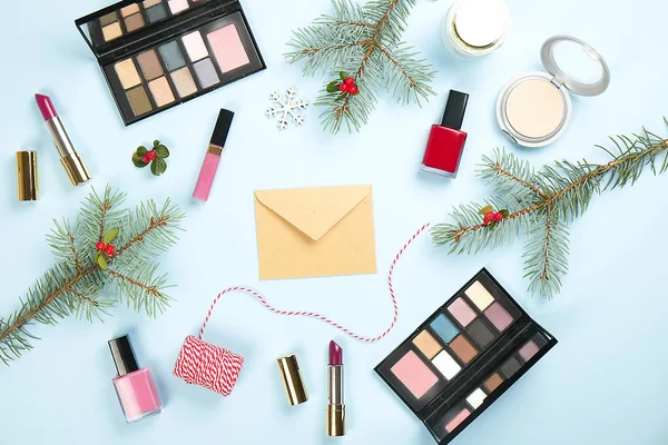 Set de produits de maquillage avec décor de Noël et enveloppe artisanale sur fond bleu plat — Photo