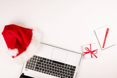Çalışma alanıyla laptop ve Noel hediye ve santa şapka beyaz zemin üzerinde yatıyordu, en iyi görünüm, kopya alanı düz. İş Noel tatil kavramı, tatil online alışveriş