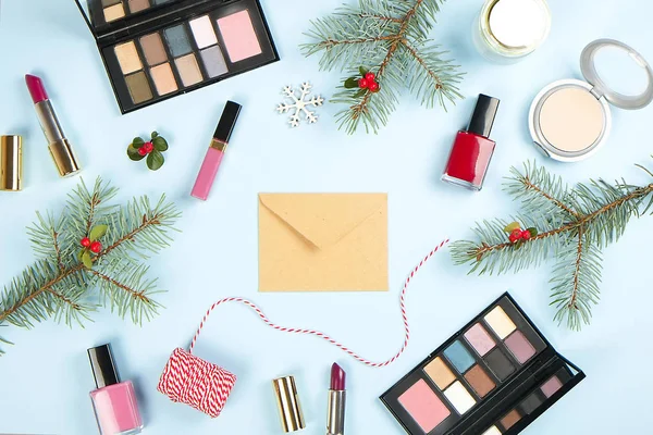 Set de produits de maquillage avec décor de Noël et enveloppe artisanale sur fond bleu plat — Photo
