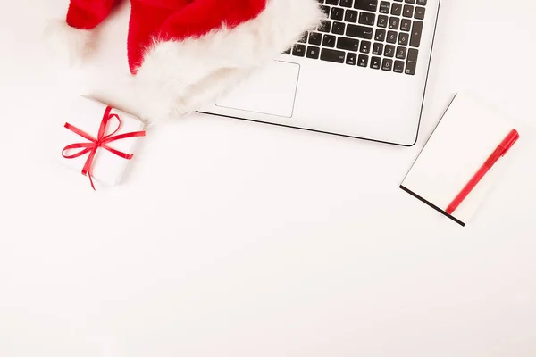 Робоче місце з кавою, ноутбуком, різдвяним подарунком та капелюхом Санти на білому тлі зверху з копіювальним простором. Концепція ділових різдвяних свят, концепція покупок в Інтернеті — стокове фото