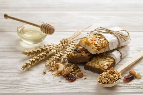 Granola superfood energy bars with almond and cashew nuts, dry fruits, raisins cherry on the white wood table, close up. Cereal superfood energy bars with mix nuts, dry fruits, raisins, chocolate, oat spikelets, honey and granola on the white wood ta