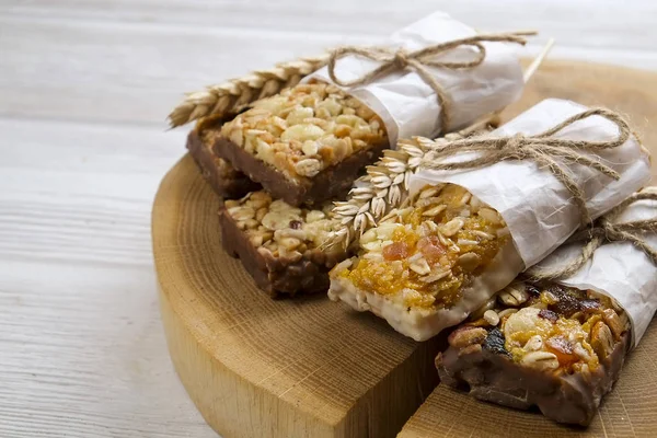 Granola superfood energy bars with almond and cashew nuts, dry fruits, raisins cherry on the white wood table, close up. Cereal superfood energy bars with mix nuts, dry fruits, raisins, chocolate, oat spikelets, honey and granola on the white wood ta