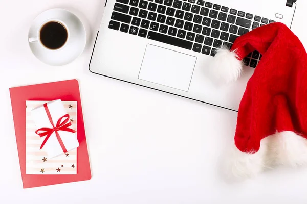 Office desk with laptop and santa hat on white background flat lay with copy space. Business christmas holidays concept, holiday online shopping concept