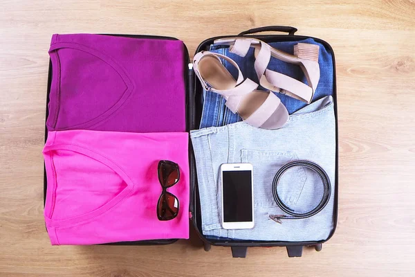 Open suitcase packed for travelling, on wooden floor top view, close up. Travel bag concept — Stock Photo, Image