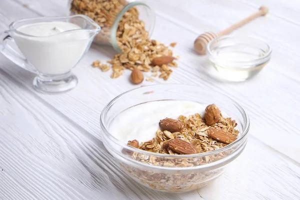 Glass bowl with Greek yogurt and mixed nuts. Healthy sports vegetarian protein rich diet, homemade granola breakfast with milk, honey, almond, cashew, hazelnut, rolled oats. Top front view, background
