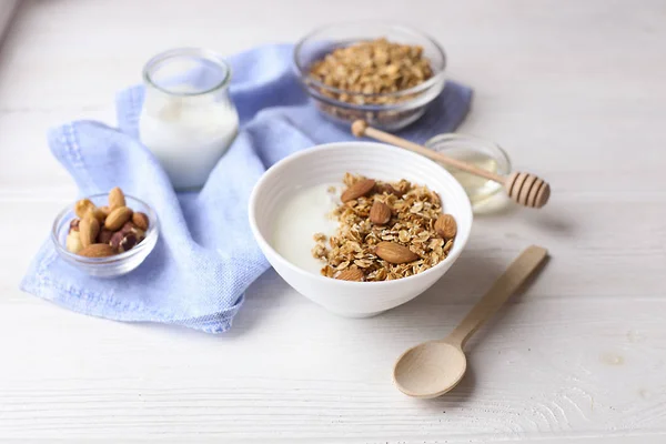 Ceramic bowl of Greek yogurt and mixed nuts. Nutritious vegetarian protein rich diet homemade breakfast with milk honey almond, cashew, hazelnut, rolled oats on white table. Top front view, background