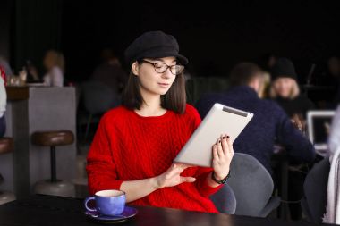 mutlu genç kadın kahve içme / çay ve tablet bilgisayara bir kafede kullanma