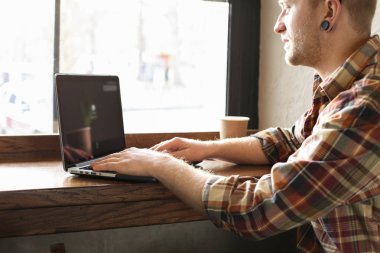 Gülümseyen sakallı işadamı giyiyor rahat hipster kahve evin içinde laptop ve cep smartphone kullanarak giyim.