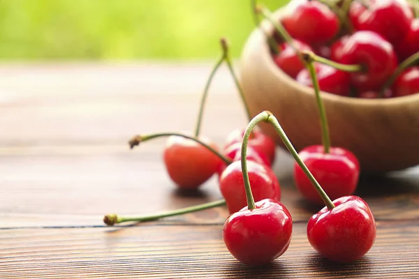 Kersen in een kom op houten oppervlak, lente / zomer, groene boom laat achtergrond. — Stockfoto