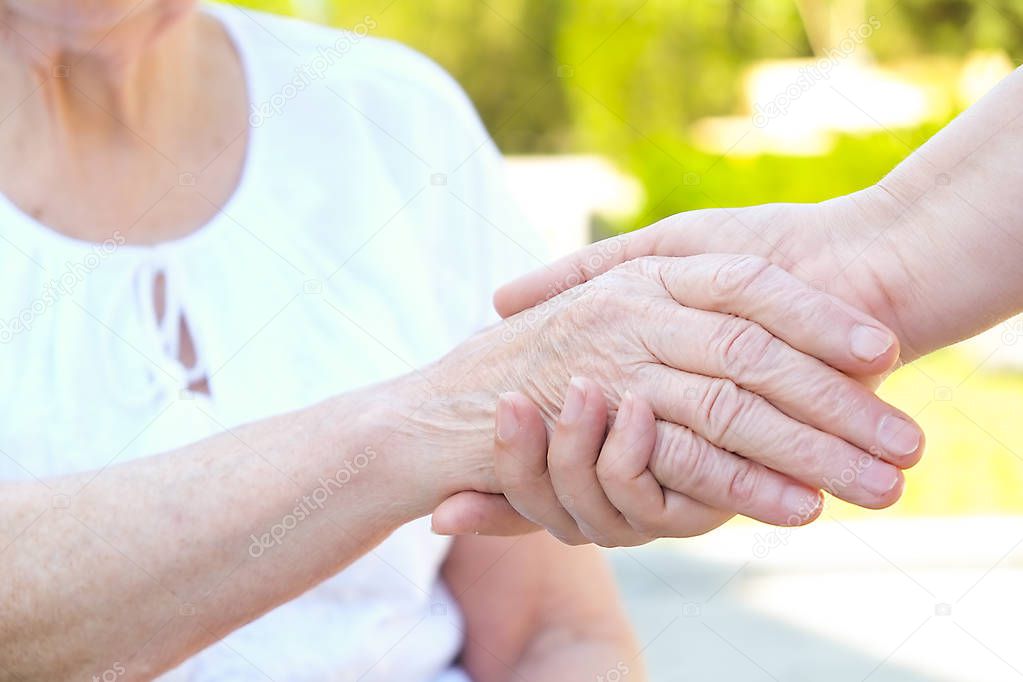 Old and young holding hands on light background close up. Helping hands, care for the elderly concept.