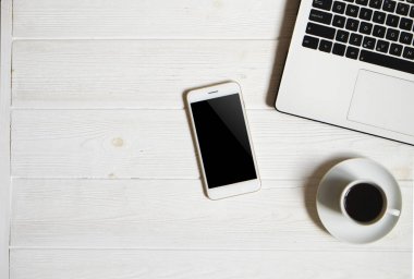 Blogger / işadamı / işkadını, bu dizüstü bilgisayar, boş ekran smartphone, kahve fincanı ve malzemeleri ile uzman'ın beyaz ahşap ofis alanı tablo. Üstten Görünüm, kopya alanı, düz lay, Tepegöz, zemin.