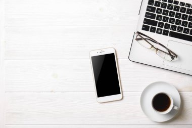 Blogger / işadamı / işkadını, bu dizüstü bilgisayar, boş ekran smartphone, kahve fincanı ve malzemeleri ile uzman'ın beyaz ahşap ofis alanı tablo. Üstten Görünüm, kopya alanı, düz lay, Tepegöz, zemin.