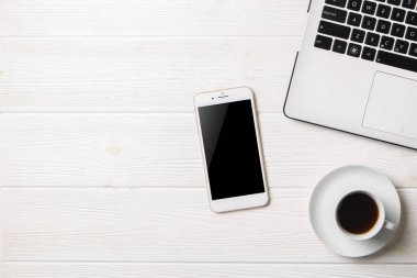 Blogger / işadamı / işkadını, bu dizüstü bilgisayar, boş ekran smartphone, kahve fincanı ve malzemeleri ile uzman'ın beyaz ahşap ofis alanı tablo. Üstten Görünüm, kopya alanı, düz lay, Tepegöz, zemin.