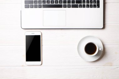 Blogger / işadamı / işkadını, bu dizüstü bilgisayar, boş ekran smartphone, kahve fincanı ve malzemeleri ile uzman'ın beyaz ahşap ofis alanı tablo. Üstten Görünüm, kopya alanı, düz lay, Tepegöz, zemin.