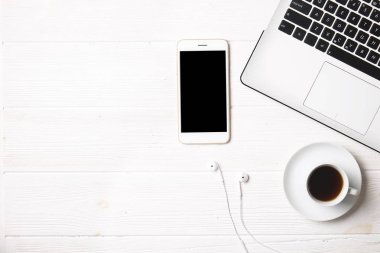 Blogger / işadamı / işkadını, bu dizüstü bilgisayar, boş ekran smartphone, kahve fincanı ve malzemeleri ile uzman'ın beyaz ahşap ofis alanı tablo. Üstten Görünüm, kopya alanı, düz lay, Tepegöz, zemin.