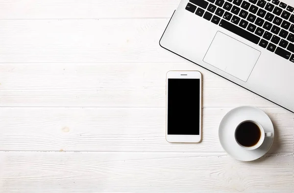 Blogger / işadamı / işkadını, bu dizüstü bilgisayar, boş ekran smartphone, kahve fincanı ve malzemeleri ile uzman'ın beyaz ahşap ofis alanı tablo. Üstten Görünüm, kopya alanı, düz lay, Tepegöz, zemin.