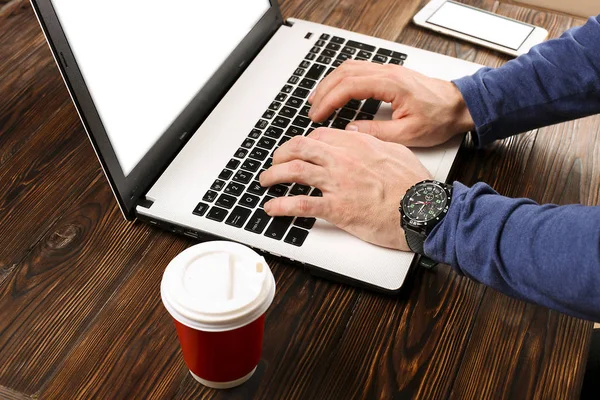 Casually dressed student / blogger / writer / man working on pc laptop, typing on keyboard, writing blog article, drinking in coffee shop / bar, using smartphone. Top view of workspace office desk.