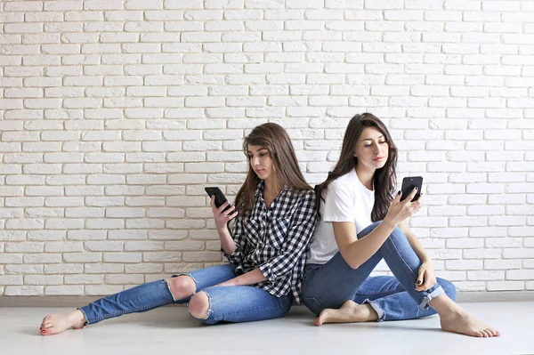 Happy millennial meninas se divertindo dentro de casa. Jovens mulheres bonitas com sorrisos carismáticos perfeitos, olhos castanhos, cabelos escuros ondulados. Interior minimalista, tijolo branco texturizado fundo de parede, estilo loft . — Fotografia de Stock