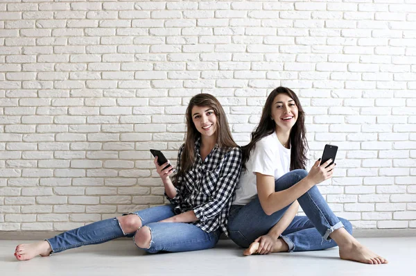 Feliz millennial niñas divirtiéndose en el interior. Mujeres hermosas jóvenes con sonrisas carismáticas perfectas, ojos marrones, cabello oscuro ondulado. Interior minimalista, fondo de pared texturizado de ladrillo blanco, estilo loft . — Foto de Stock