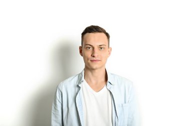 Yakışıklı genç model ayakta, beyaz duvar arka planda, geniş bir gülümseme poz. Hipster rahat sokak tarzı, düz açılarak mavi gömlek.
