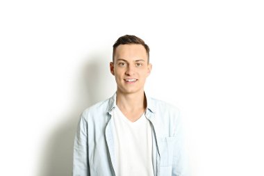 Yakışıklı genç model ayakta, beyaz duvar arka planda, geniş bir gülümseme poz. Hipster rahat sokak tarzı, düz açılarak mavi gömlek.