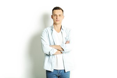 Yakışıklı genç model ayakta, beyaz duvar arka planda, geniş bir gülümseme poz. Hipster rahat sokak tarzı, düz açılarak mavi gömlek.