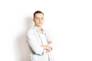 Yakışıklı genç model ayakta, beyaz duvar arka planda, geniş bir gülümseme poz. Hipster rahat sokak tarzı, düz açılarak mavi gömlek.