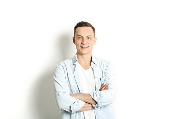 Handsome young man model standing, posing on white wall background, wide smile. Hipster casual street style, plain unbuttoned baby blue shirt.