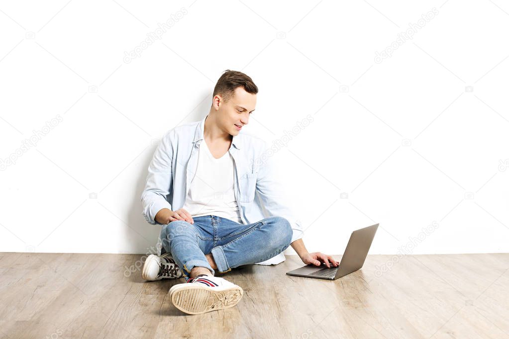 Handsome young man model sitting, posing on white wall background, wide smile. Hipster casual street style, plain unbuttoned baby blue shirt.