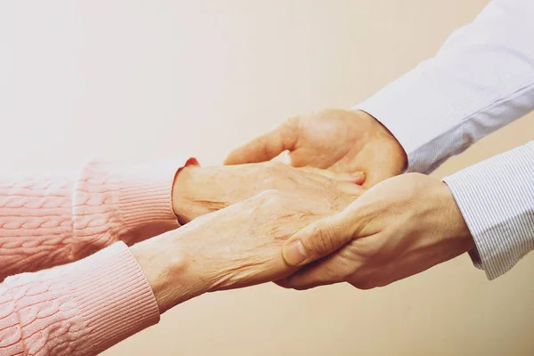 stock image Mature female in elderly care facility gets help from hospital personnel nurse. Close up of aged wrinkled hands of senior woman. Grand mother everyday life.