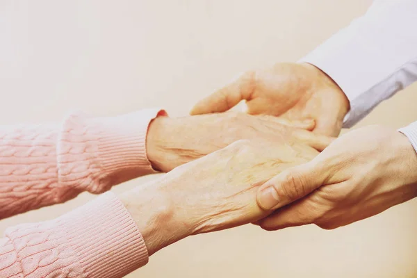 Rijpe vrouw in ouderen zorg faciliteit krijgt hulp van ziekenhuis personeel verpleegkundige. Close up van leeftijd gerimpelde handen van senior vrouw. Grand moeder dagelijks leven. — Stockfoto