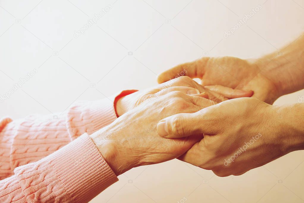 Mature female in elderly care facility gets help from hospital personnel nurse. Close up of aged wrinkled hands of senior woman. Grand mother everyday life.