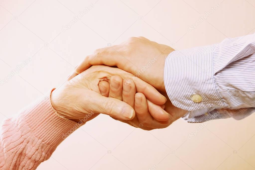 Mature female in elderly care facility gets help from hospital personnel nurse. Close up of aged wrinkled hands of senior woman. Grand mother everyday life.