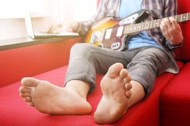 Raslantı genç adam gitar şarkıları evde odada ile giyinmiş. Online gitar dersleri kavramı. Erkek gitarist pratik akor kulpları.