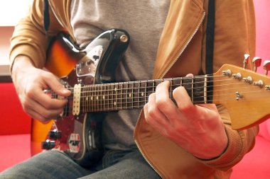 Raslantı genç adam gitar şarkıları evde odada ile giyinmiş. Online gitar dersleri kavramı. Erkek gitarist pratik akor kulpları.