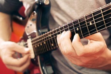 Raslantı genç adam gitar şarkıları evde odada ile giyinmiş. Online gitar dersleri kavramı. Erkek gitarist pratik akor kulpları.