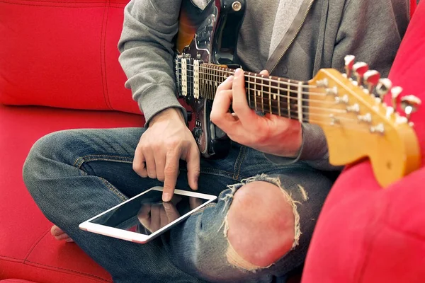 Casually dressed young man with guitar playing songs in the room at home. Online guitar lessons concept. Male guitarist practicing chord grips.